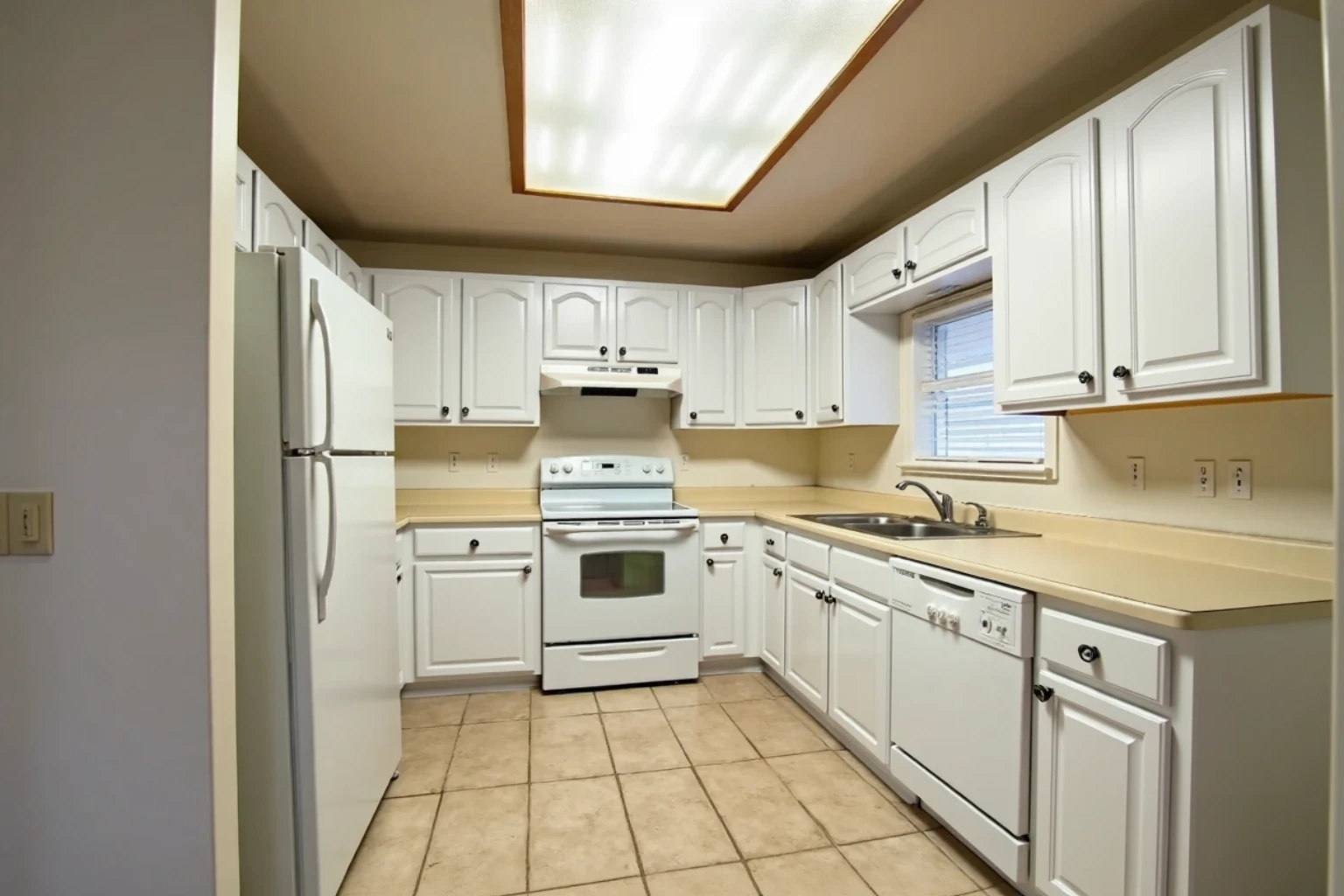 The same kitchen with its arched doors and drawer fronts now white, small dark knobs, room otherwise unchanged.