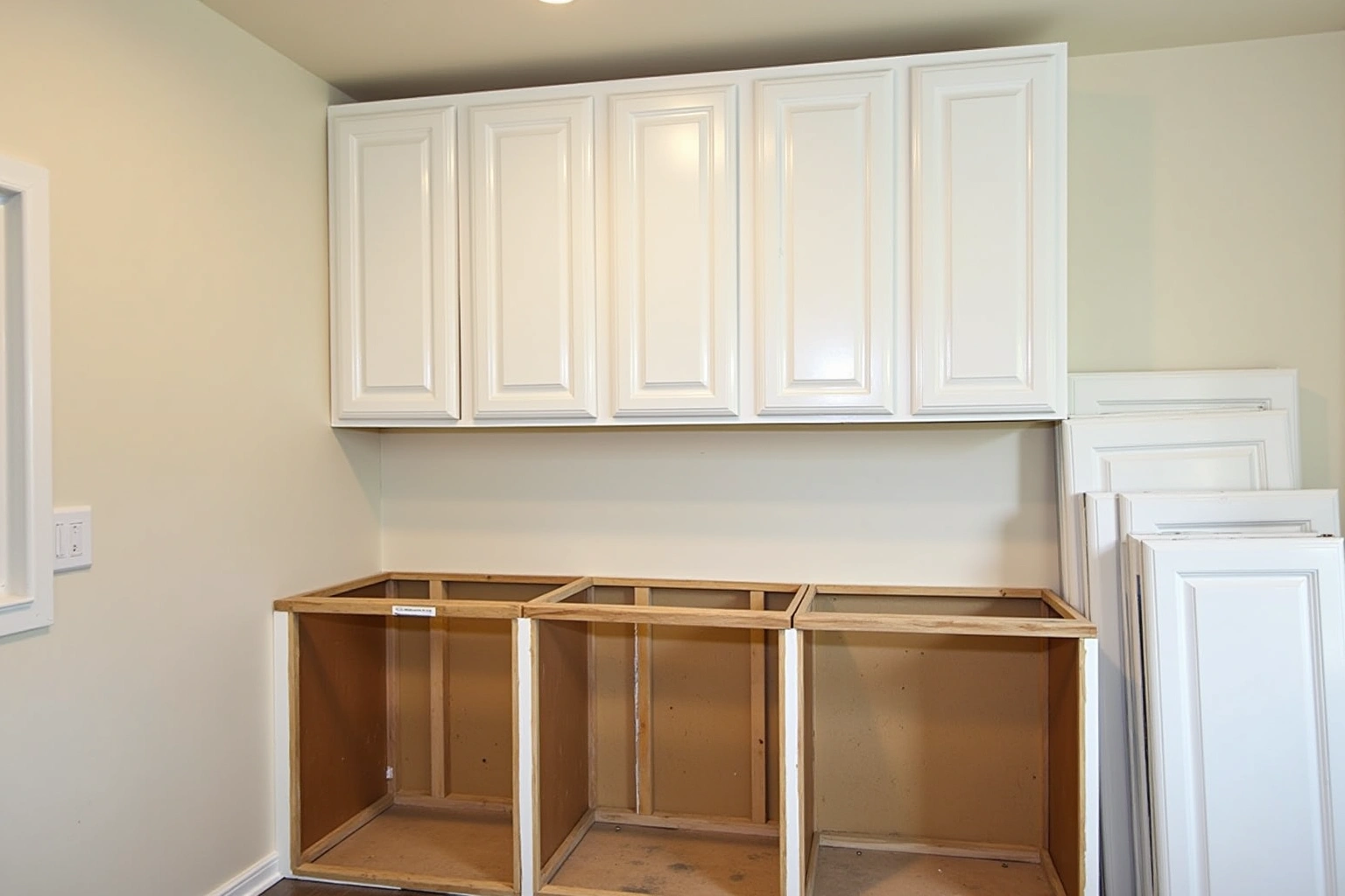 Refacing in progress with new white doors hung on the uppers, bare base boxes below and spare doors stacked beside.